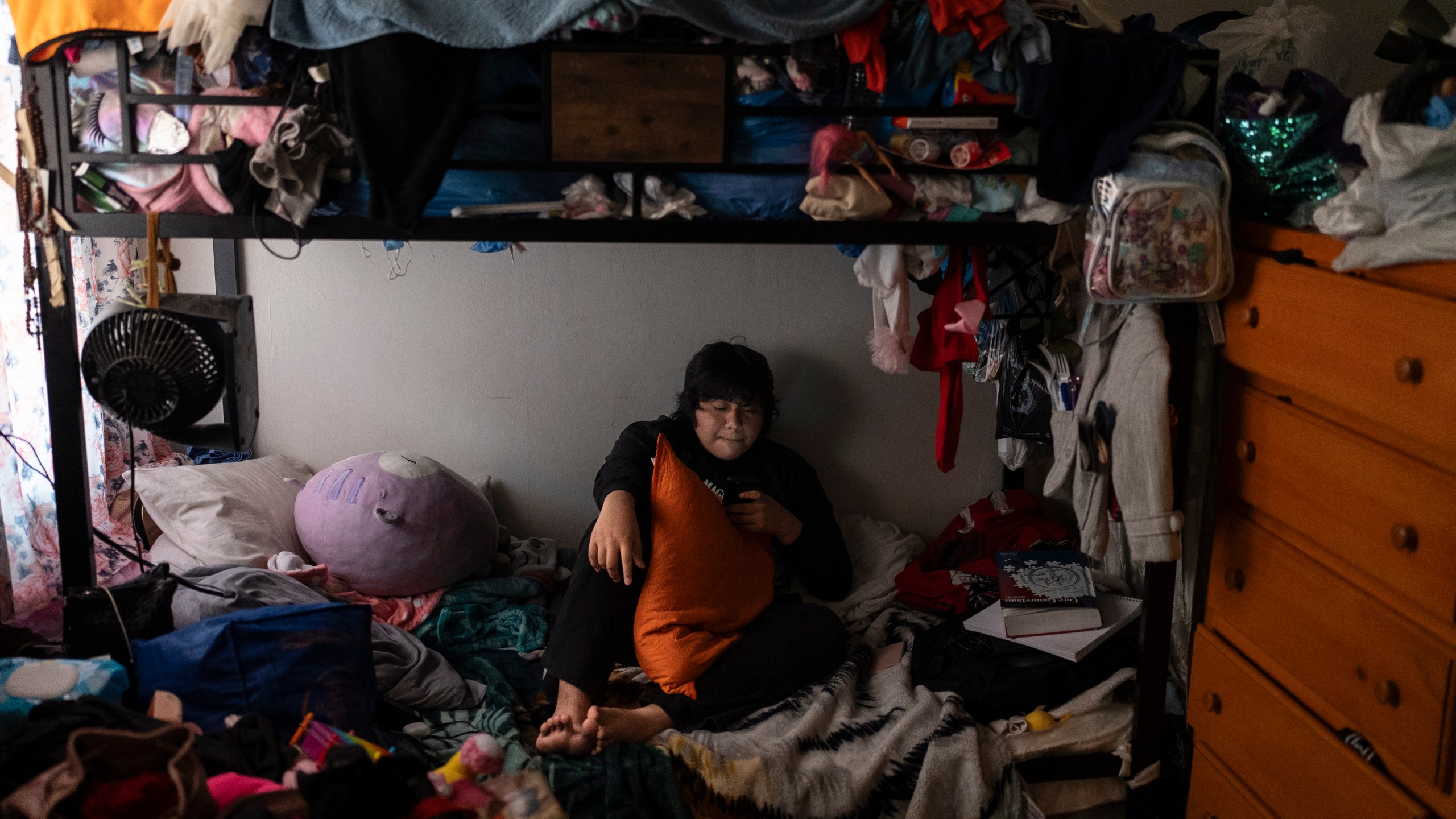 Deneffy Sánchez, 15, rests on a bed he shares with his mother and little sister just feet away from their roommate's bed in Los Angeles, Saturday, Sept. 9, 2023. In Los Angeles, housing insecurity is one of the biggest reasons kids have missed school since the pandemic and struggle to catch up. (AP Photo/Jae C. Hong)