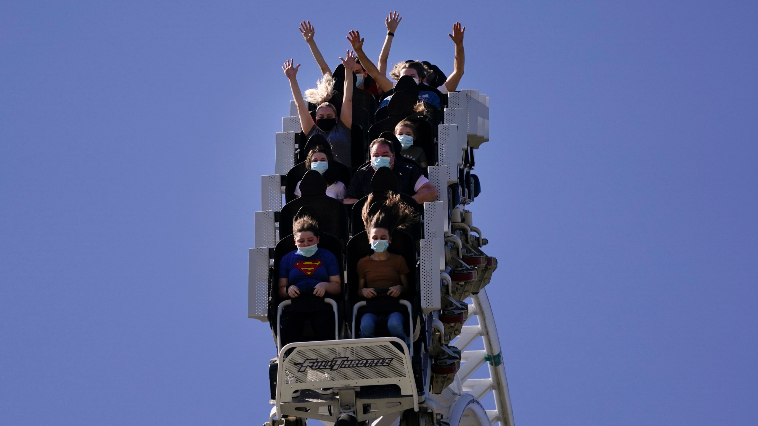 FILE - Visitors wearing masks ride on a roller coaster at Six Flags Magic Mountain on its first day of reopening to members and pass holders in Valencia, Calif., on April 1, 2021. Cedar Fair and Six Flags Entertainment Corp. are merging, creating an expansive amusement park operator with operations spread across 17 states and three countries. (AP Photo/Jae C. Hong, File)